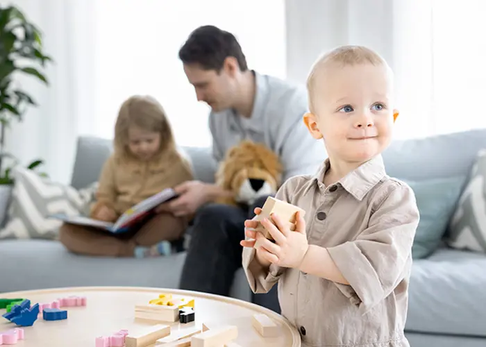 Mies lukee sohvalla kirjaa lapselle ja toinen lapsi leikkii palikoilla. 